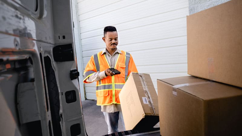 ims-industry-images Delivery worker in a high-visibility vest scanning a large cardboard box near a delivery van.